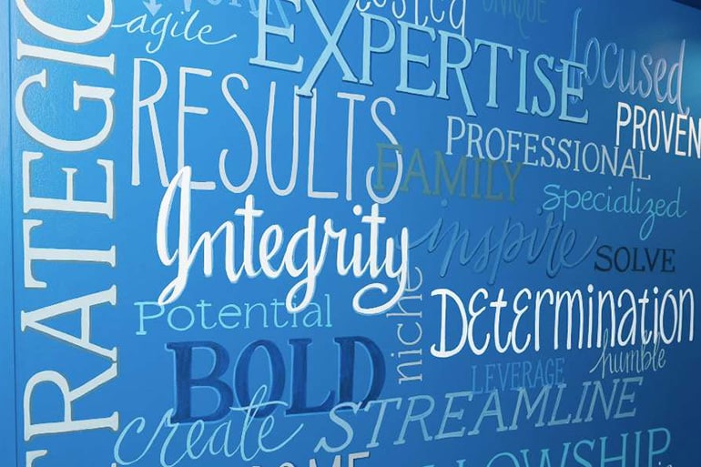 A blue wall filled with various motivational words in different fonts and sizes, including "Expertise," "Results," "Integrity," "Determination," and "Professional.