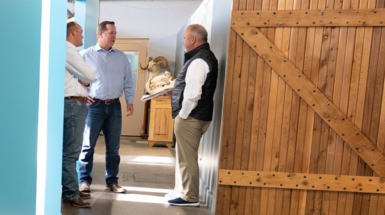 Three men are standing and conversing in a hallway next to a wooden sliding door.