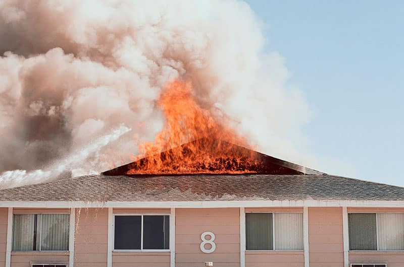 A fire engulfs the roof of a building with the number 8 visible on the exterior, producing thick smoke against a clear sky.